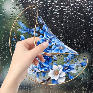 Close-up of static cling window film featuring blue flowers and a dragonfly on a rainy pane