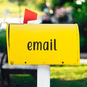 Vintage yellow metal mailbox with red flag and email lettering in a garden setting