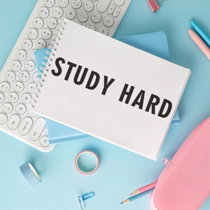 Spiral notebook with STUDY HARD text, pens and colorful stationery on light blue background