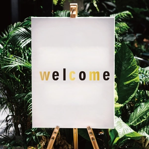 Artistic welcome canvas sign on wooden easel surrounded by lush green tropical plants