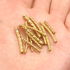 Macro shot of gold stainless steel tube beads with diamond pattern on a palm