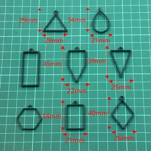 Matte black geometric DIY alloy pendants in various shapes on a green cutting mat