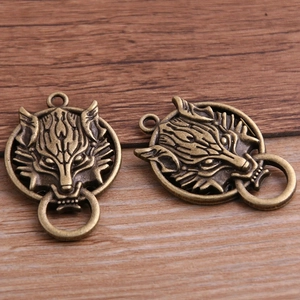 Pair of vintage bronze wolf head alloy charms with loops on brown wooden surface