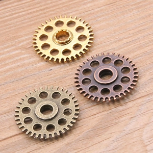 Three assorted steampunk alloy gear pendants in gold and bronze on a wooden background