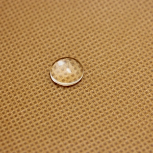 Macro shot of a clear round glass cabochon showing transparency on brown grid texture