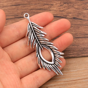 Detailed macro view of an antique silver hollow peacock feather pendant held in hand