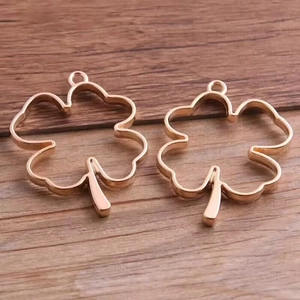 Two rose gold clover shaped hollow pendant charms for DIY jewelry on wood background