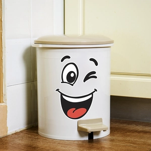 Pedal trash can with funny cartoon smiley face sticker on a light wood floor background