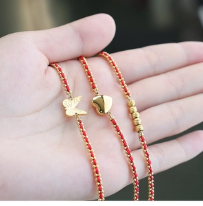 Detalle de pulseras trenzadas rojas con dijes dorados de mariposa y corazón en mano