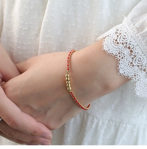 Primer plano de pulsera de cordón rojo trenzado con cuentas de oro en muñeca mujer