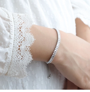 Detalle de una pulsera tenis de plata con circonitas sobre fondo de encaje blanco