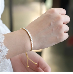 Detalle de pulsera tenis dorada ajustable con circonitas cúbicas en una muñeca femenina
