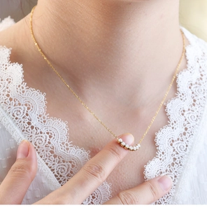 Detalle de un collar tennis dorado con 7 piedras de circonita sobre top de encaje