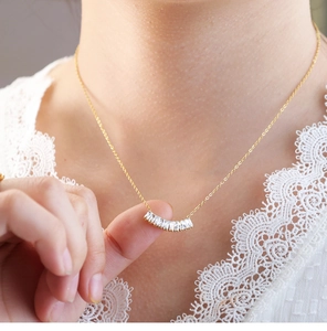 Detalle de elegante collar dorado con colgante curvo de circonitas cúbicas con corte tipo baguette