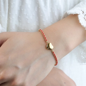Pulsera artesanal de cuerda roja con colgante de corazón dorado en la muñeca