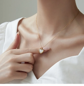 Detalle de un collar de oro en forma de corazón con nácar blanco en el cuello de una modelo