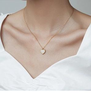 Primer plano de un collar con colgante de corazón de nácar blanco y cadena dorada fina