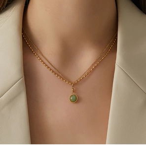 Detail of double-layer gold necklace with green gemstone pendant on model neck