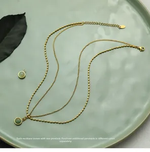 Macro detail of a layered gold necklace with a round green agate pendant on a ceramic tray