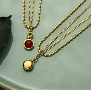 Detailed close-up of a double-layered gold necklace with a red agate pendant on a plate
