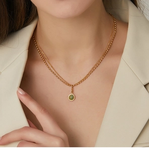 Detailed view of layered gold necklace with green stone pendant on white suit