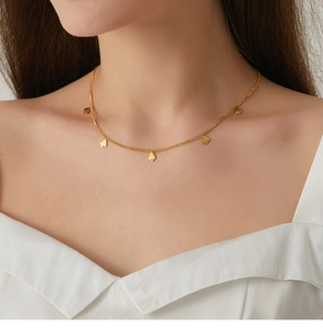 Detalle de collar dorado con colgantes de picas sobre una blusa de seda blanca