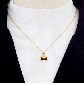 Detail of gold chain necklace with black quilted purse pendant on white knitwear
