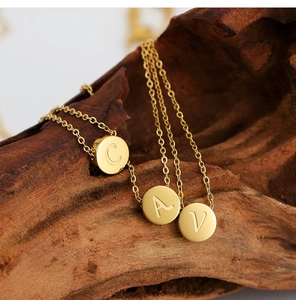 Primer plano de collares de acero inoxidable bañados en oro de 18K con letras A C V grabadas