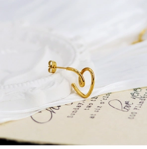 Nahaufnahme der minimalistischen hohlen herzförmigen Goldstecker auf Seidenhintergrund