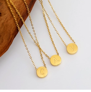 Detalle de tres collares de acero chapado en oro 18K con discos grabados con letras C, A, V