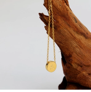 Detalle del collar con mini disco bañado en oro de 18K y letra A grabada sobre madera