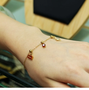 Detail of gold chain bracelet with red gemstone, star charm and wavy enamel pendant