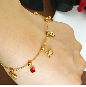 Detail of gold bracelet featuring star charm, number nine, and red heart gemstone