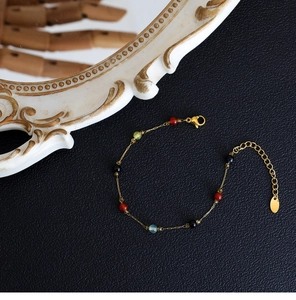 Detail of 18K gold-plated necklace with colorful gemstones on black leather background