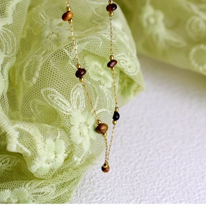 Close-up of handmade 18K gold-plated chain with tiger eye beads on lace fabric