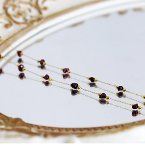 Macro shot of 18K gold chain with amethyst and tiger eye stone beads on mirror