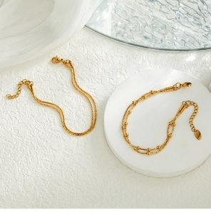 Detail view of double-layer gold snake chain bracelet with bead charms and lobster clasp