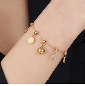 Detail of gold bracelet featuring Fu character charm, small bell and crescent moon pendant