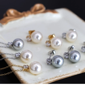 Detail of gray pearl pendant and stud earrings set on a white ceramic jewelry tray