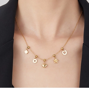 Detail of gold stainless steel necklace with LUCK clover and star pendants on a model
