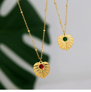Close-up of gold monstera leaf necklace pendants with green and red center gemstones