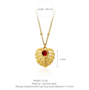 Detail view of gold monstera leaf pendant necklace with red gemstone and size dimensions