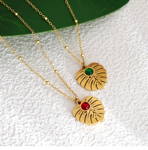 Detailed view of monstera leaf pendants with green and red gems on gold satellite chains