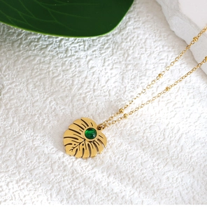 Detail of gold monstera leaf pendant with green gemstone on beaded chain necklace