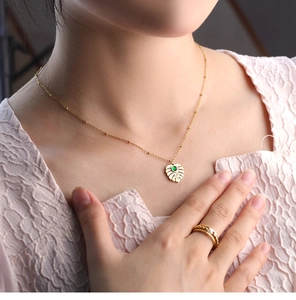 Golden leaf pendant necklace with green gemstone and beaded chain on female model