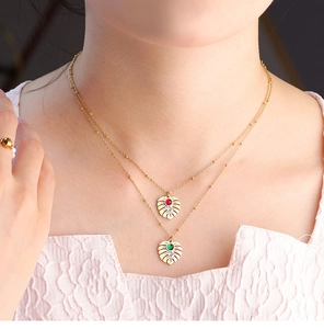 Detail of layered gold monstera leaf necklace with red and green charms on model