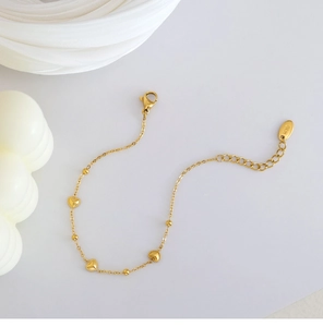Macro shot of 18K gold plated heart pendants and round beads on a steel bracelet