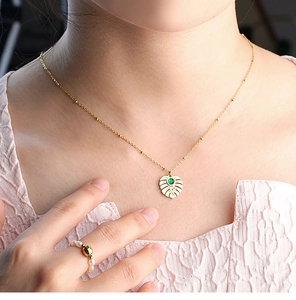 Detail of gold tropical leaf necklace with green gemstone and beaded chain on a model