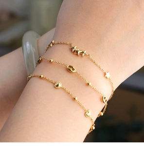 Detailed close-up of layered 18K gold-plated bracelets featuring stars, hearts and beads