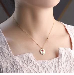 Detail of gold tropical monstera leaf pendant with red stone on a beaded satellite chain